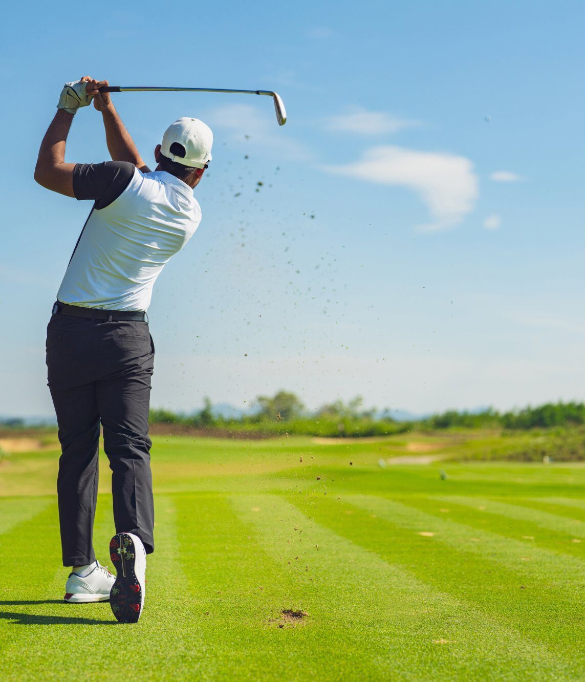 Golfer hitting a long drive against a blue sky